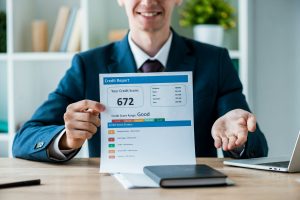 selective focus of cheerful man holding document with credit report lettering near laptop in office